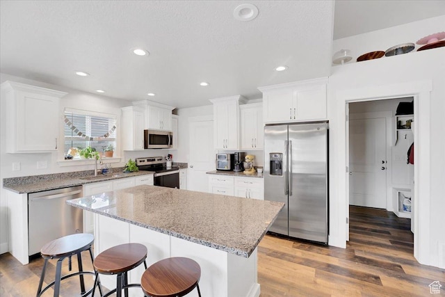 kitchen with a center island, a sink, appliances with stainless steel finishes, wood finished floors, and a breakfast bar area