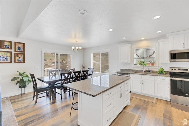 kitchen with a chandelier, light wood-style flooring, white cabinetry, appliances with stainless steel finishes, and a sink