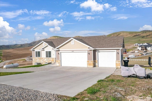 view of front of home with driveway, a garage, stone siding, a mountain view, and central AC unit