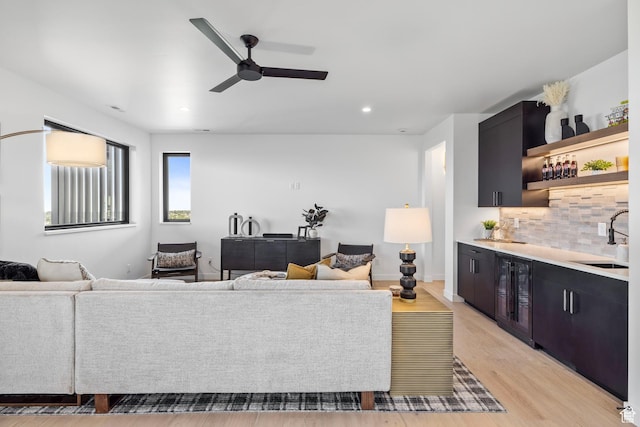 living room featuring ceiling fan, indoor wet bar, light wood-style flooring, recessed lighting, and beverage cooler