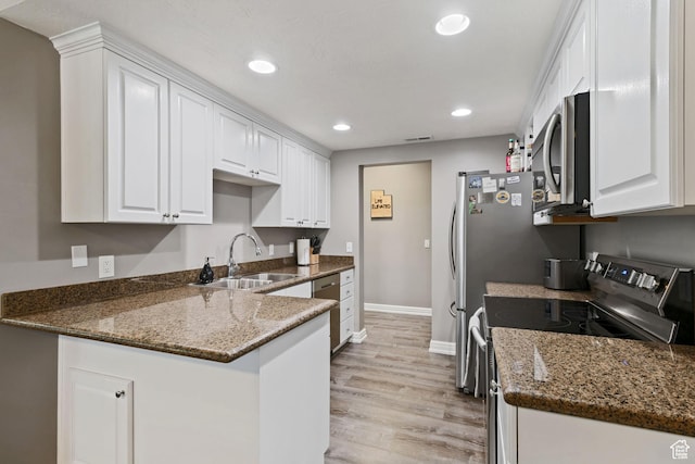 kitchen with baseboards, a peninsula, white cabinets, appliances with stainless steel finishes, and a sink