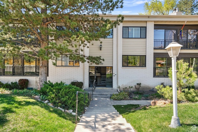 townhome / multi-family property with brick siding, a chimney, and a front lawn