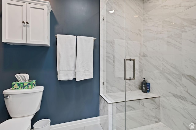 bathroom with toilet, baseboards, and a marble finish shower