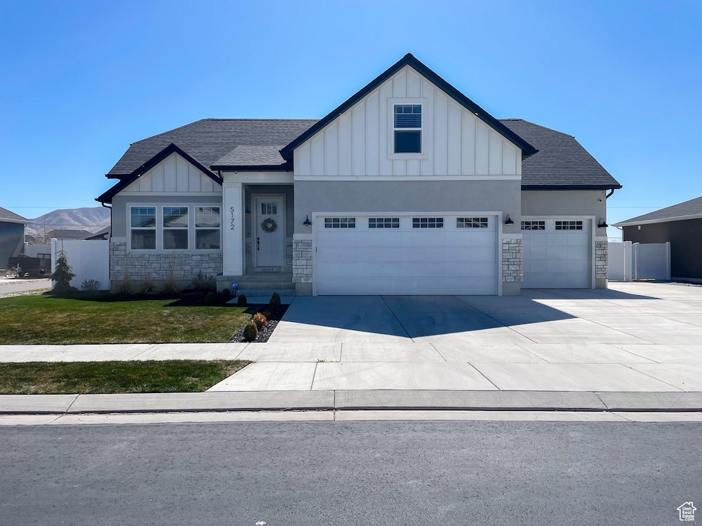 view of front of property featuring concrete driveway, board and batten siding, stone siding, an attached garage, and fence