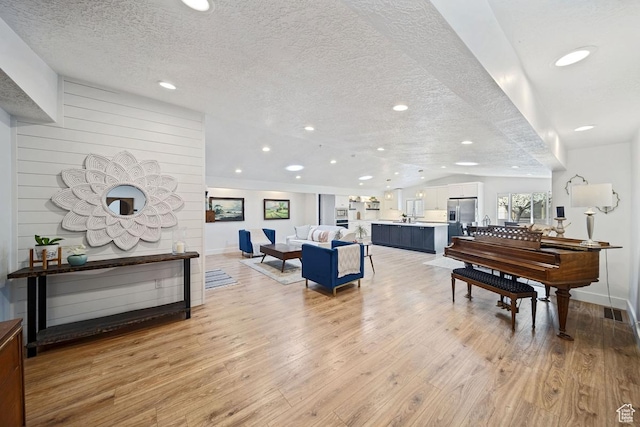 living room featuring visible vents, baseboards, a textured ceiling, light wood finished floors, and recessed lighting