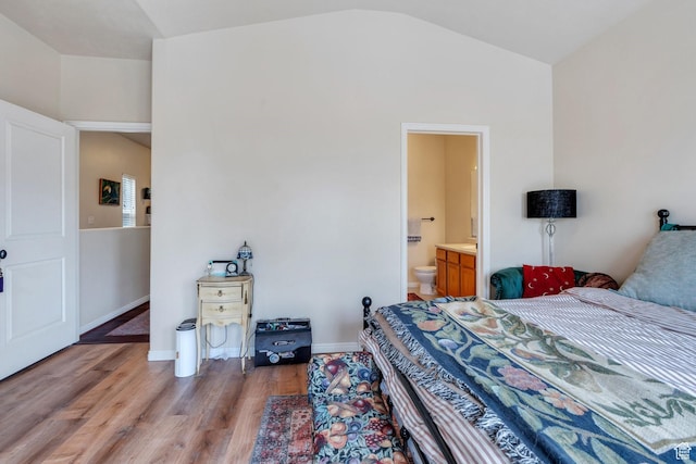 bedroom featuring baseboards, light wood-type flooring, ensuite bath, and vaulted ceiling