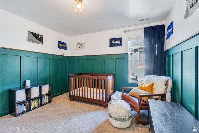 carpeted bedroom featuring a decorative wall, visible vents, and a wainscoted wall