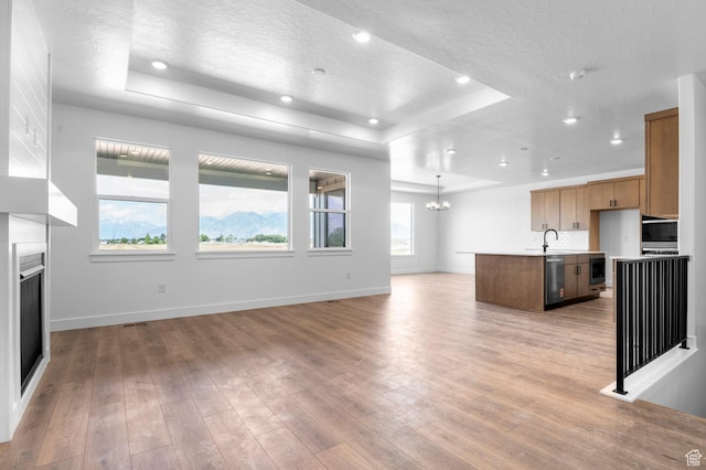 1489 E 820 N Unit 104, Salem, UT 84653 - unfurnished living room with a tray ceiling, a textured ceiling, a glass covered fireplace, light wood-style flooring, and a chandelier