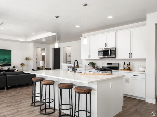 kitchen with white cabinets, open floor plan, appliances with stainless steel finishes, a breakfast bar, and dark wood finished floors