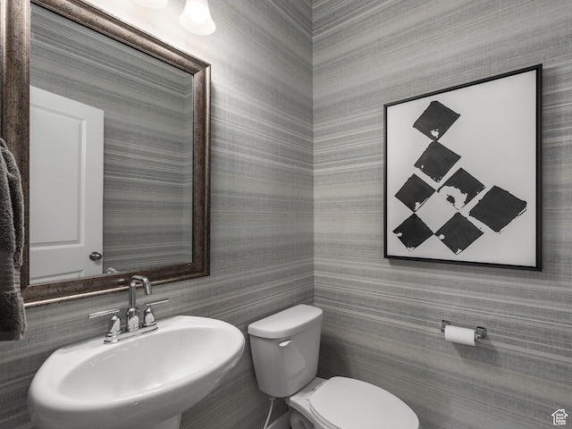 bathroom with toilet, wallpapered walls, and a sink