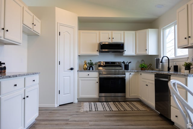 kitchen with a sink, light wood-type flooring, appliances with stainless steel finishes, white cabinetry, and light stone countertops