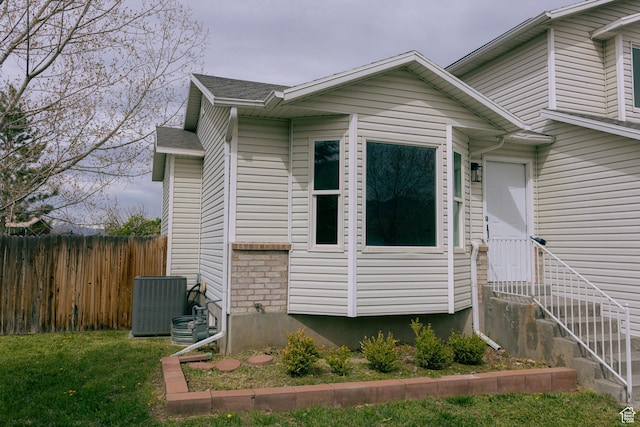 view of home's exterior with roof with shingles, central air condition unit, entry steps, a yard, and fence