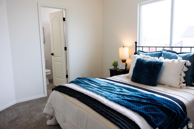carpeted bedroom featuring ensuite bath and baseboards