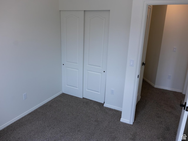 unfurnished bedroom with a closet, dark colored carpet, and baseboards