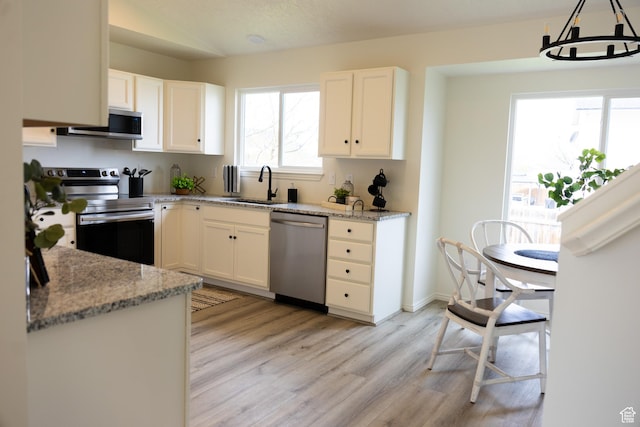 kitchen with appliances with stainless steel finishes, light wood finished floors, a sink, and white cabinetry