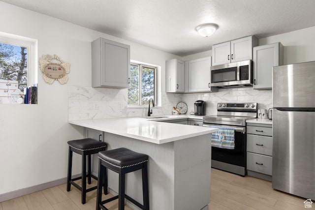 kitchen with gray cabinets, a peninsula, a sink, and stainless steel appliances