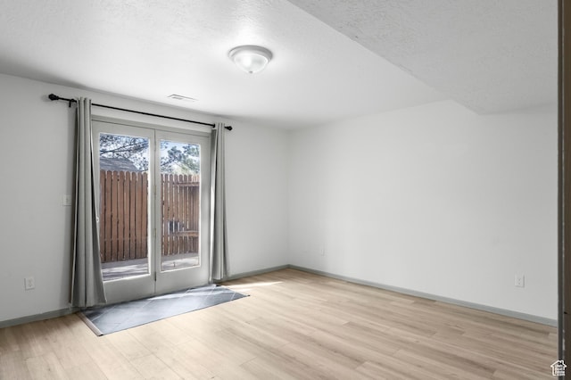 unfurnished room featuring baseboards, visible vents, light wood-type flooring, and a textured ceiling
