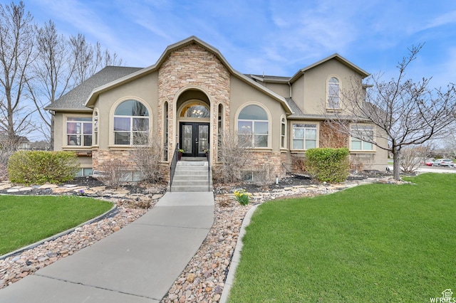 view of front of house featuring stucco siding, stone siding, a front lawn, french doors, and a shingled roof