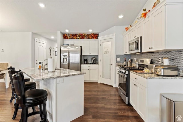 kitchen with white cabinets, light stone countertops, dark wood-type flooring, decorative backsplash, and appliances with stainless steel finishes