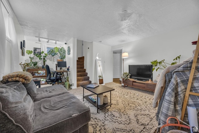 carpeted living room with stairway, a textured ceiling, and track lighting