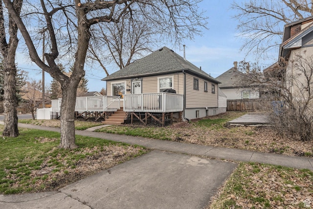 view of front facade with fence, a wooden deck, and roof with shingles