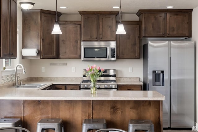 kitchen with dark brown cabinets, light countertops, a sink, hanging light fixtures, and stainless steel appliances
