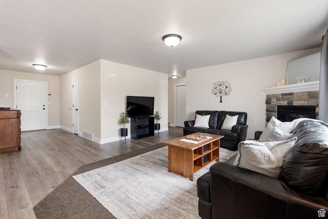 living room with light wood-style floors, visible vents, baseboards, and a stone fireplace