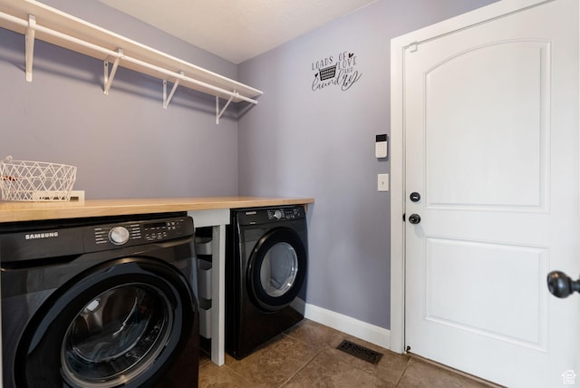 clothes washing area with laundry area, dark tile patterned flooring, visible vents, washer and dryer, and baseboards