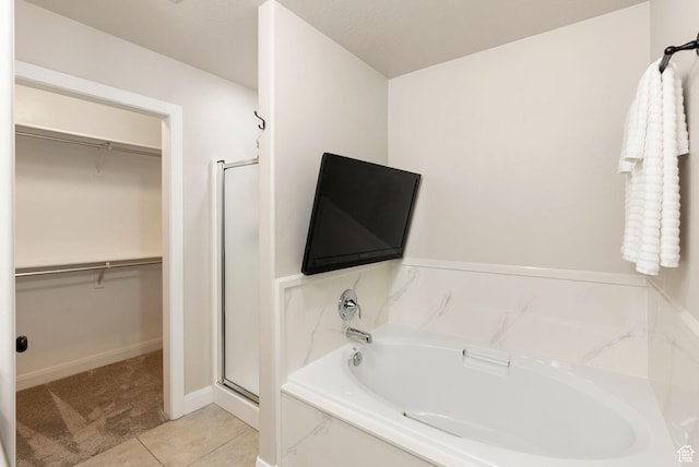 bathroom with baseboards, a stall shower, tile patterned floors, a walk in closet, and a garden tub
