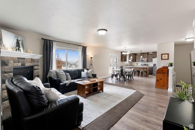 living room featuring baseboards, a chandelier, a textured ceiling, a fireplace, and light wood-style flooring