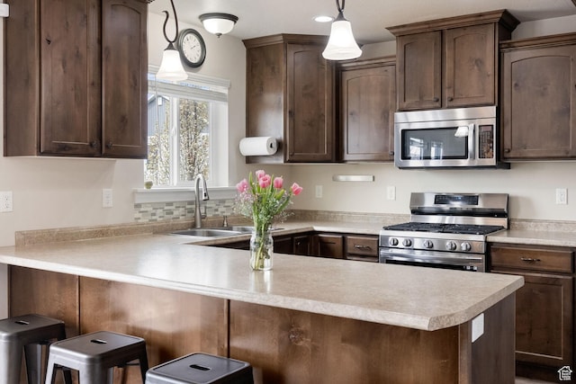 kitchen featuring pendant lighting, a peninsula, dark brown cabinets, light countertops, and stainless steel appliances