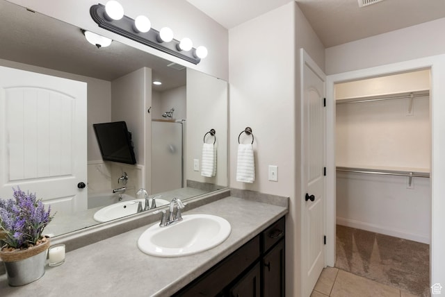 full bath featuring tile patterned flooring, vanity, a walk in closet, and a stall shower