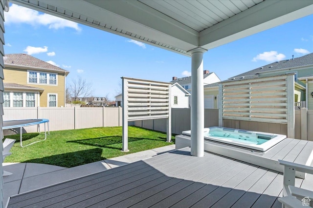 wooden deck featuring a yard, a fenced backyard, a trampoline, and an outdoor hot tub