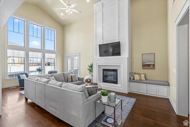 living room featuring dark wood-style flooring, baseboards, a large fireplace, a ceiling fan, and high vaulted ceiling