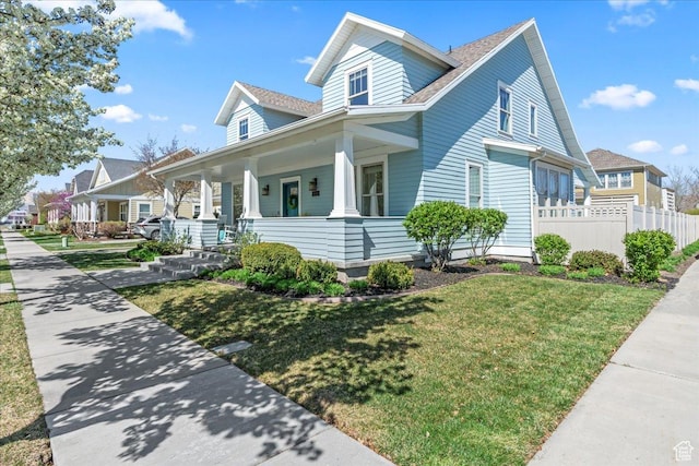 view of front facade with covered porch, a front yard, and fence