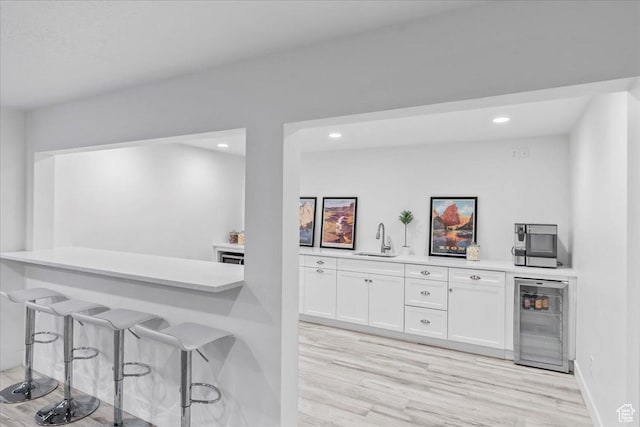 bar featuring light wood-style flooring, wine cooler, and a sink