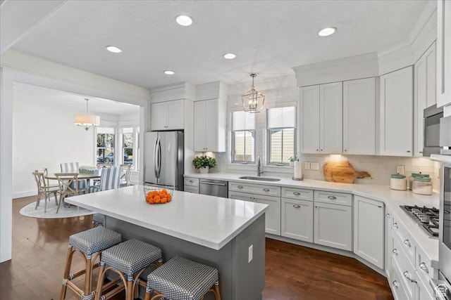kitchen featuring a kitchen bar, appliances with stainless steel finishes, a sink, light countertops, and decorative backsplash