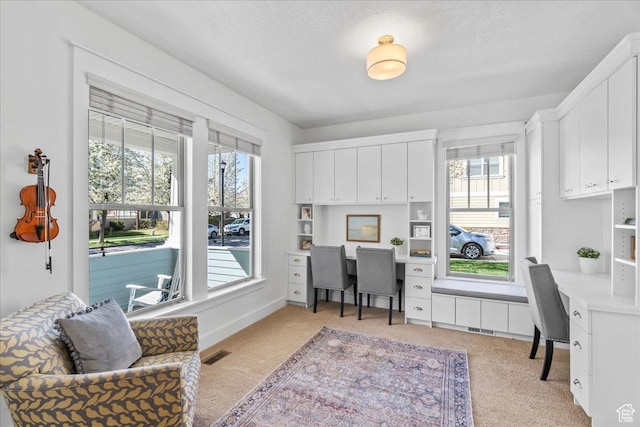 office featuring a healthy amount of sunlight, light colored carpet, built in study area, and visible vents