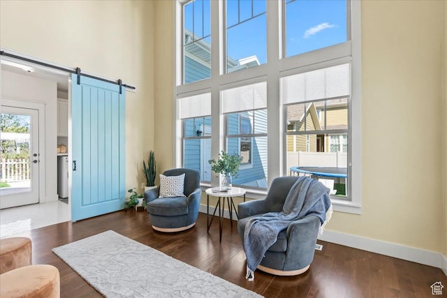 living area with a barn door, a high ceiling, baseboards, and wood finished floors