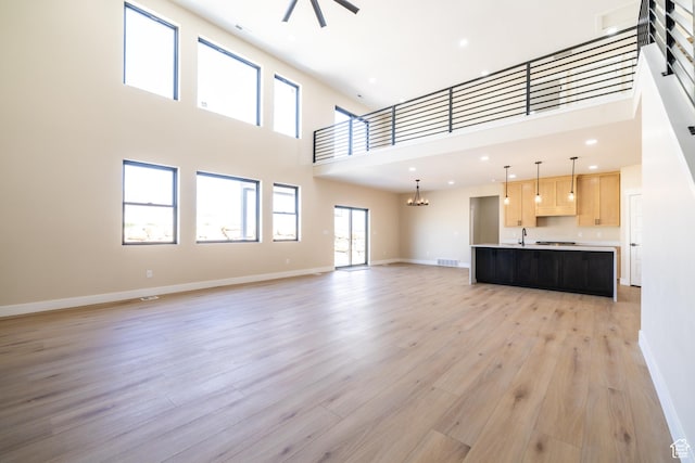 2899 E Lake Dr, Eagle Mountain, UT 84005 - unfurnished living room featuring light wood-style floors, a towering ceiling, visible vents, a sink, and baseboards