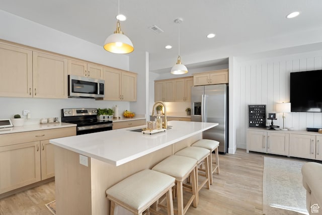 kitchen with appliances with stainless steel finishes, a sink, light wood finished floors, light brown cabinetry, and a breakfast bar