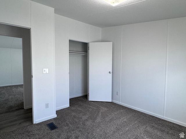 unfurnished bedroom with dark carpet and a closet