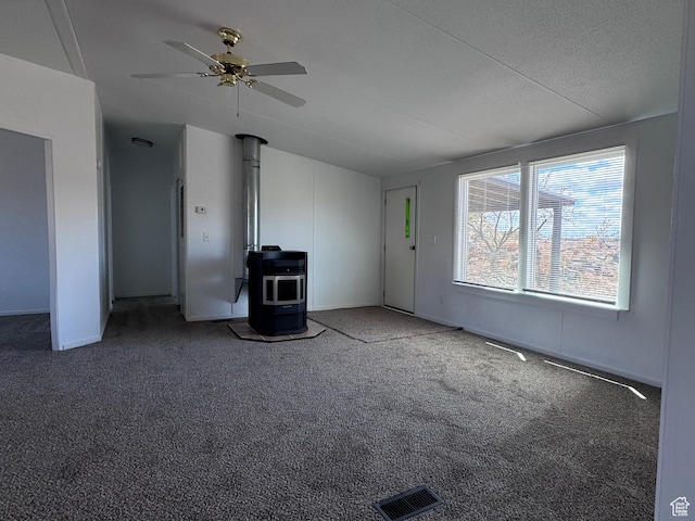 unfurnished living room with a wood stove, lofted ceiling, a ceiling fan, and carpet flooring
