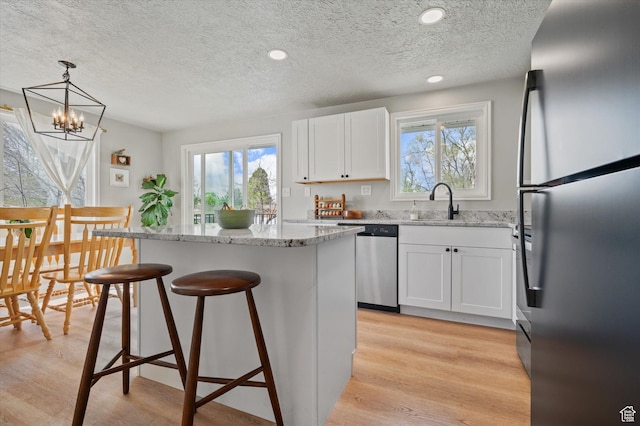 1308 Gilman Dr, Layton, UT 84040 - kitchen with a breakfast bar, light stone counters, white cabinetry, a center island, and appliances with stainless steel finishes