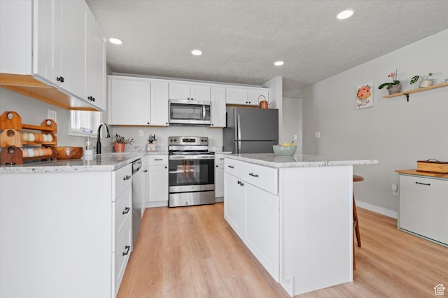 1308 Gilman Dr, Layton, UT 84040 - kitchen with light wood-style floors, a center island, a textured ceiling, appliances with stainless steel finishes, and white cabinetry