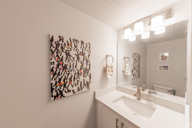 half bath with vanity, a textured ceiling, and toilet