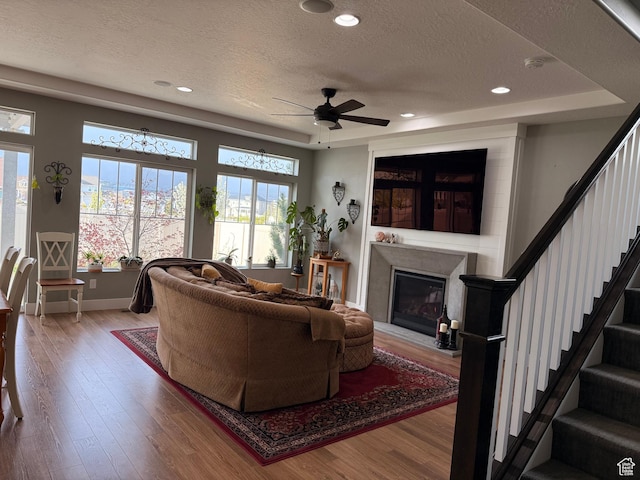 living area with ceiling fan, a textured ceiling, baseboards, and light wood-type flooring