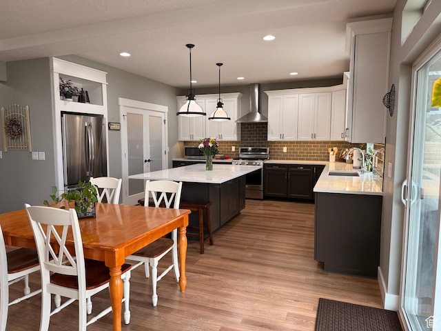 kitchen featuring a sink, a kitchen island, wall chimney range hood, light wood-style floors, and stainless steel appliances