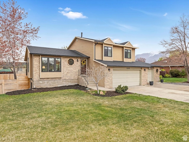 split level home featuring brick siding, driveway, a front yard, and fence