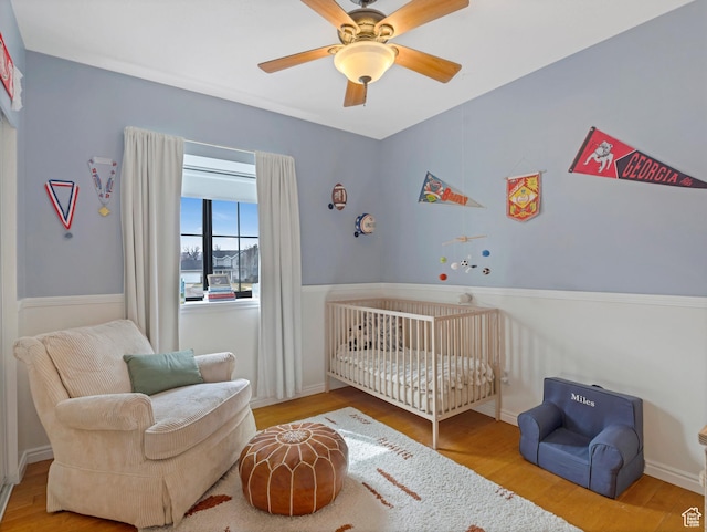 bedroom with a crib, wood finished floors, and ceiling fan